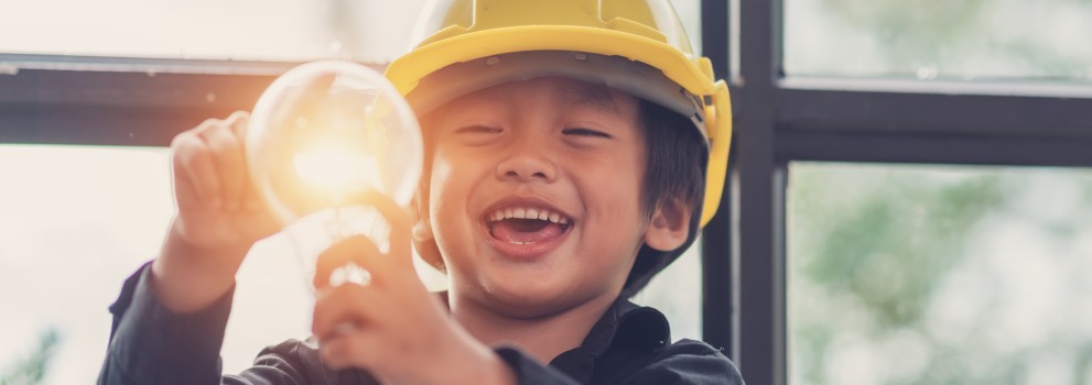 A child wearing a safety helmet holds a light bulb. A child wearing a safety helmet holds a light bulb.