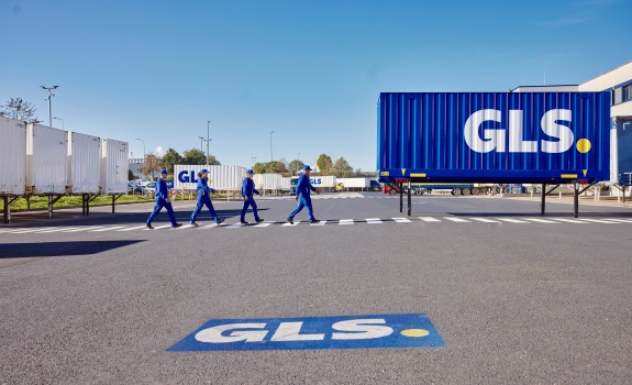 GLS employees walking outside depot on crosswalk and there is a blue color GLS swap body behind them.