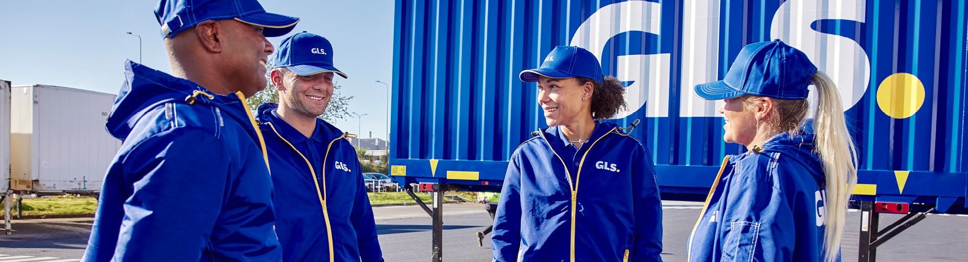 GLS employees in professional uniforms at a logistics site, standing in front of a transport container, illustrating parcel delivery services and last-mile logistics.