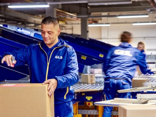 Employees sort and scan parcels on a conveyor belt.