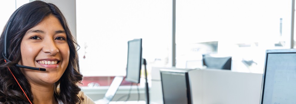 Smiling customer support agent wearing a headset at a computer.